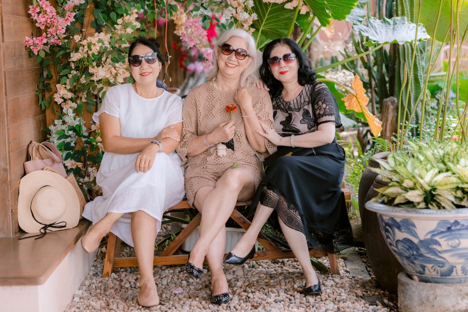 Three stylish women seated outdoors among lush plants, enjoying a sunny day with smiles.